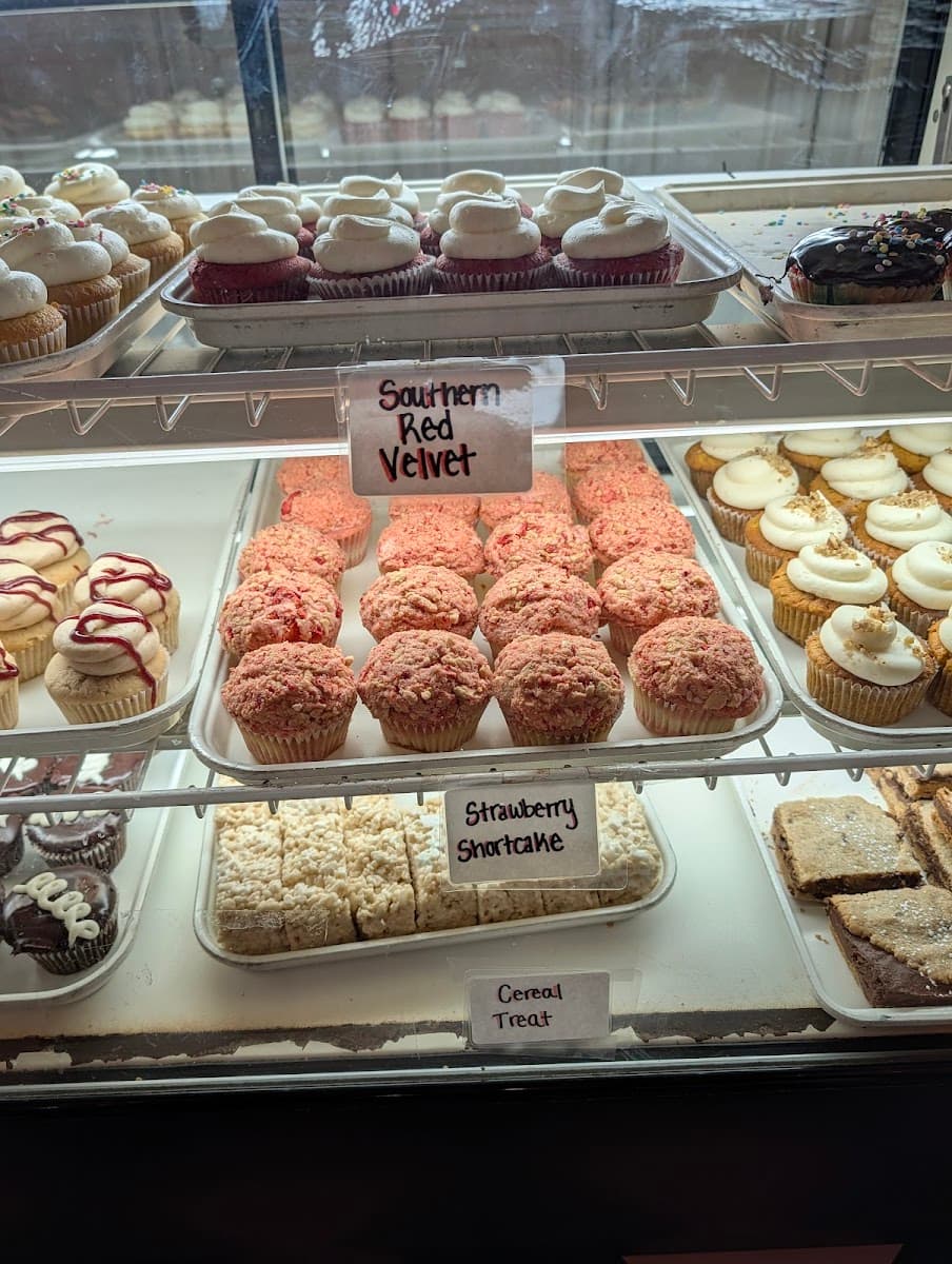 A white bakery tray holds an assortment of pastries, including a sugar doughnut, hot dog bun, and savory pork floss bread in front of a display case.