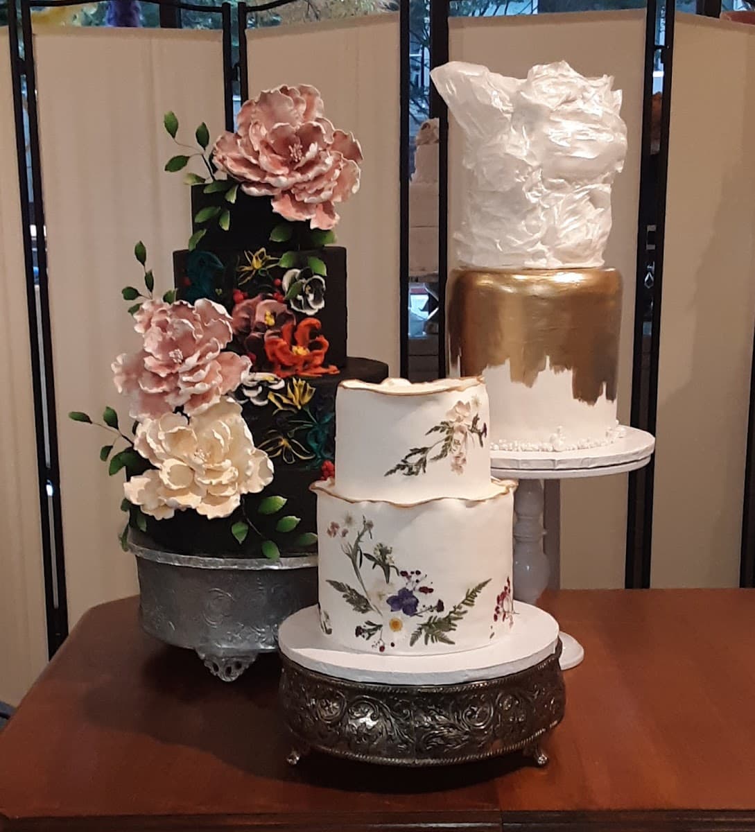 A whimsical five-tier wedding cake with a brown tree bark base, a green leafy tier featuring a golden keyhole, a white tier with a forest scene behind black gates, and a pink top tier personalized with names and adorned with red, white, and peach roses.