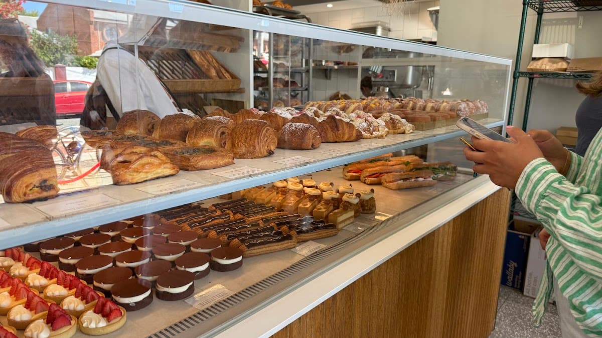 A white bakery tray holds an assortment of pastries, including a sugar doughnut, hot dog bun, and savory pork floss bread in front of a display case.