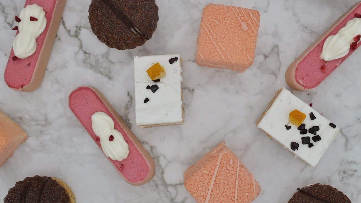 A white bakery tray holds an assortment of pastries, including a sugar doughnut, hot dog bun, and savory pork floss bread in front of a display case.